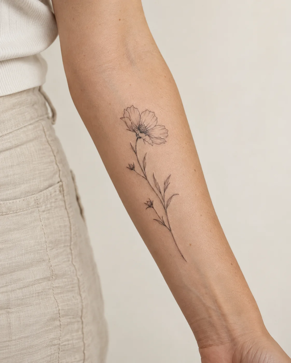 Fine-line wildflower tattoo on an inner forearm